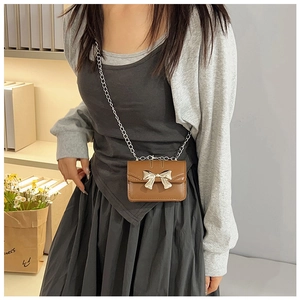 Detail of caramel mini crossbody bag with a silver metal bow and fine chain strap