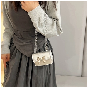 Detail shot of mini silver crossbody bag featuring a golden bow metal buckle and chain strap