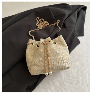 Détail de broderie florale sur sac seau en paille beige avec chaîne dorée et perles