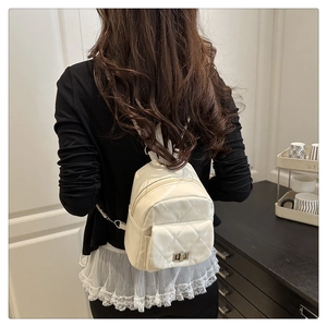 Close-up of white quilted mini backpack featuring a silver metal twist lock on the front pocket
