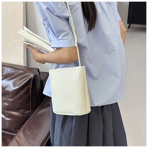 Detail of ivory woven textured bucket bag with braided shoulder strap on model