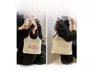Detail of straw tote bag showing handheld and shoulder carry styles with Hello embroidery