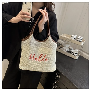 Detail of woven beige tote bag featuring red Hello embroidery and brown leather handles