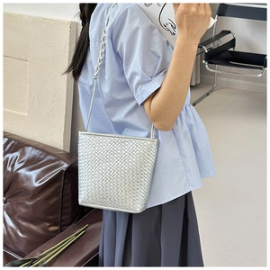 Close-up of a silver woven bucket bag featuring intricate braided leather straps