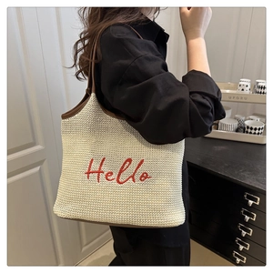 Detailed close-up of woven straw tote bag with red Hello embroidery and leather straps