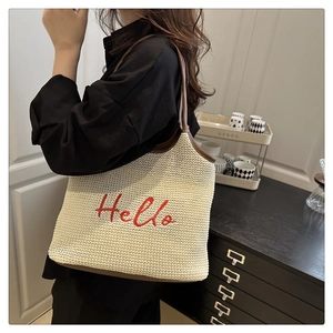 Close-up of beige woven tote bag with red Hello embroidery and brown leather trim
