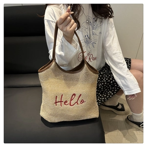 Detail of woven straw tote bag featuring red Hello embroidery and brown leather handles