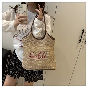 Close-up of beige woven tote bag with red Hello embroidery and brown leather handles