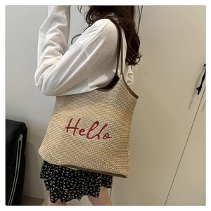 Detail of straw woven tote bag with Hello embroidery and dark brown leather straps