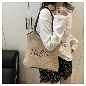 Detail of a straw tote bag with red Hello embroidery and brown leather trim handles