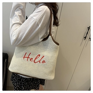 Detail of red Hello embroidery on straw tote bag with brown leather handles