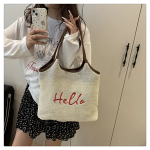 Detailed view of straw woven tote bag with red Hello embroidery and leather handles