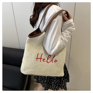Detail of embroidered Hello lettering on a woven straw tote bag with brown leather straps