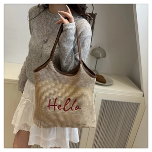 Detail of red Hello embroidery on straw woven tote bag with brown leather handles