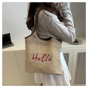 Detail view of woven straw tote bag with red Hello embroidery and leather handles