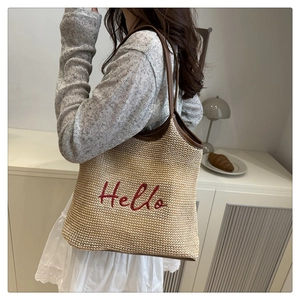 Straw tote bag with red Hello embroidery and brown leather straps worn by a model