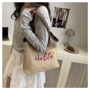 Detail of embroidered 'Hello' text on a summer straw tote bag with brown leather straps