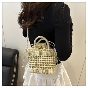 Detail of beige hollow-out straw crossbody bag with drawstring liner and long shoulder strap