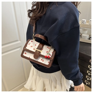Woman carrying a white crossbody bag with cherry prints and brown leather trim