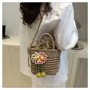 Detail of woven straw shoulder bag featuring decorative knit flowers and drawstring lining