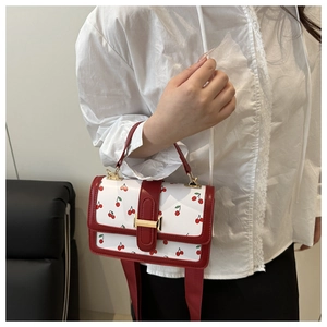 Détail du sac à bandoulière blanc à motif cerise avec anse rouge et fermoir doré