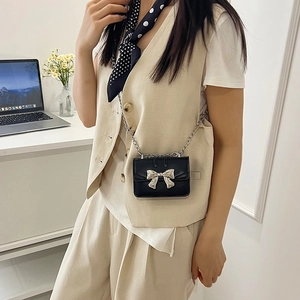 Mini black crossbody chain bag with silver bow accent, styled on a model in a modern office