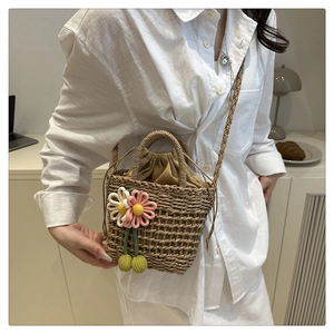 Close-up of handmade straw bucket bag featuring crochet flower charms and drawstring liner