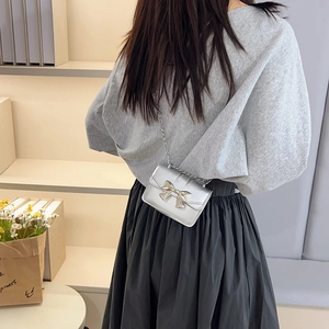 Silver mini square crossbody bag with metallic bow and chain strap on female model