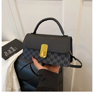 Detail of a black crossbody bag with grey M letter prints and a golden twist lock closure
