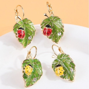 Élégantes boucles d'oreilles feuilles avec coccinelles rouges et jaunes sur fond orange