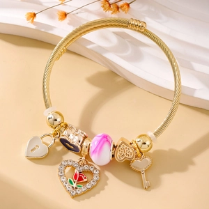 Detailed macro of a gold cable bracelet with romantic heart and rose charms on a stone base
