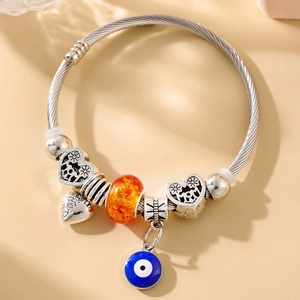 Detail of silver twisted bracelet with orange bead, heart charms and evil eye pendant