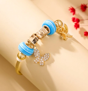 Close-up of golden beaded bracelet featuring butterfly and dragonfly charms with blue beads