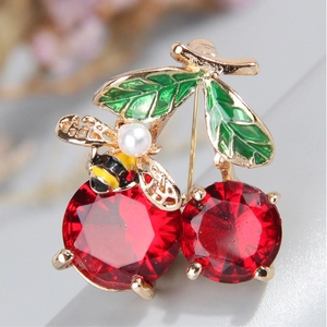 Macro detail of cherry brooch with red crystals, green enamel leaf, and a small bee with pearl