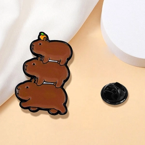 Broche en émail design capybara empilé avec petite orange sur fond de tissu drapé