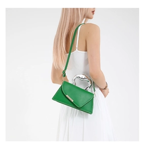 Green leather handbag with metallic handle and white stitching worn by a model