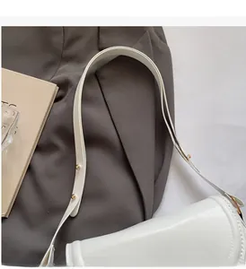 Détail du sac à bandoulière en cuir blanc avec rivets dorés sur fond de costume gris