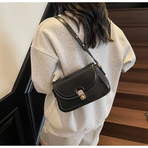 Détail d'un sac à bandoulière en cuir noir avec fermoir doré porté par un modèle