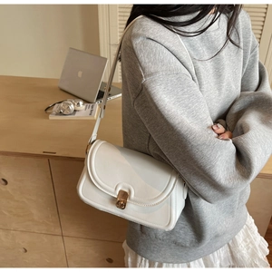 Détail du sac à bandoulière en cuir blanc avec fermoir en métal doré sur bureau bois