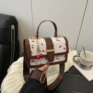 White cherry print crossbody bag with brown handles and a gold buckle in a tea setting