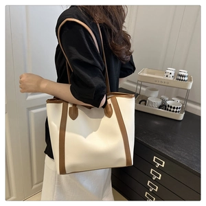 Side view of a large cream and brown color-block tote bag worn by a model in a room