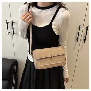 Detail of a beige leather crossbody bag featuring a unique gold horseshoe metal buckle
