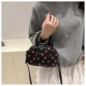 Modèle portant un mini sac cabas noir imprimé cerises avec poignées et bandoulière