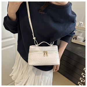 Close-up of white woven leather texture with dual gold zippers on a stylish crossbody bag