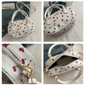 Close-up of golden zipper detail and cherry print pattern on white leather crossbody bag