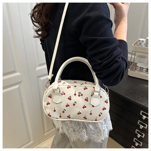 Detail of red cherry print pattern on white synthetic leather shoulder bag with golden hooks