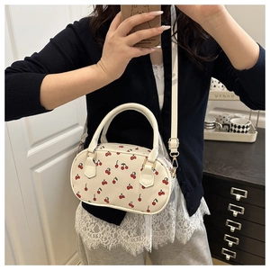 Close-up of a white shoulder bag with red cherry print and golden hardware details