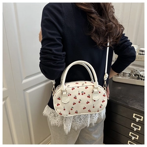 Detail shot of a white crossbody bowling bag with red cherry prints and golden hardware