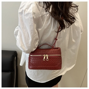 Macro detail of wine red woven box bag featuring dual gold zippers and smooth leather strap