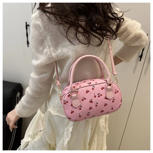 Detail view of pink cherry print crossbody bag worn by model in an indoor lifestyle setting